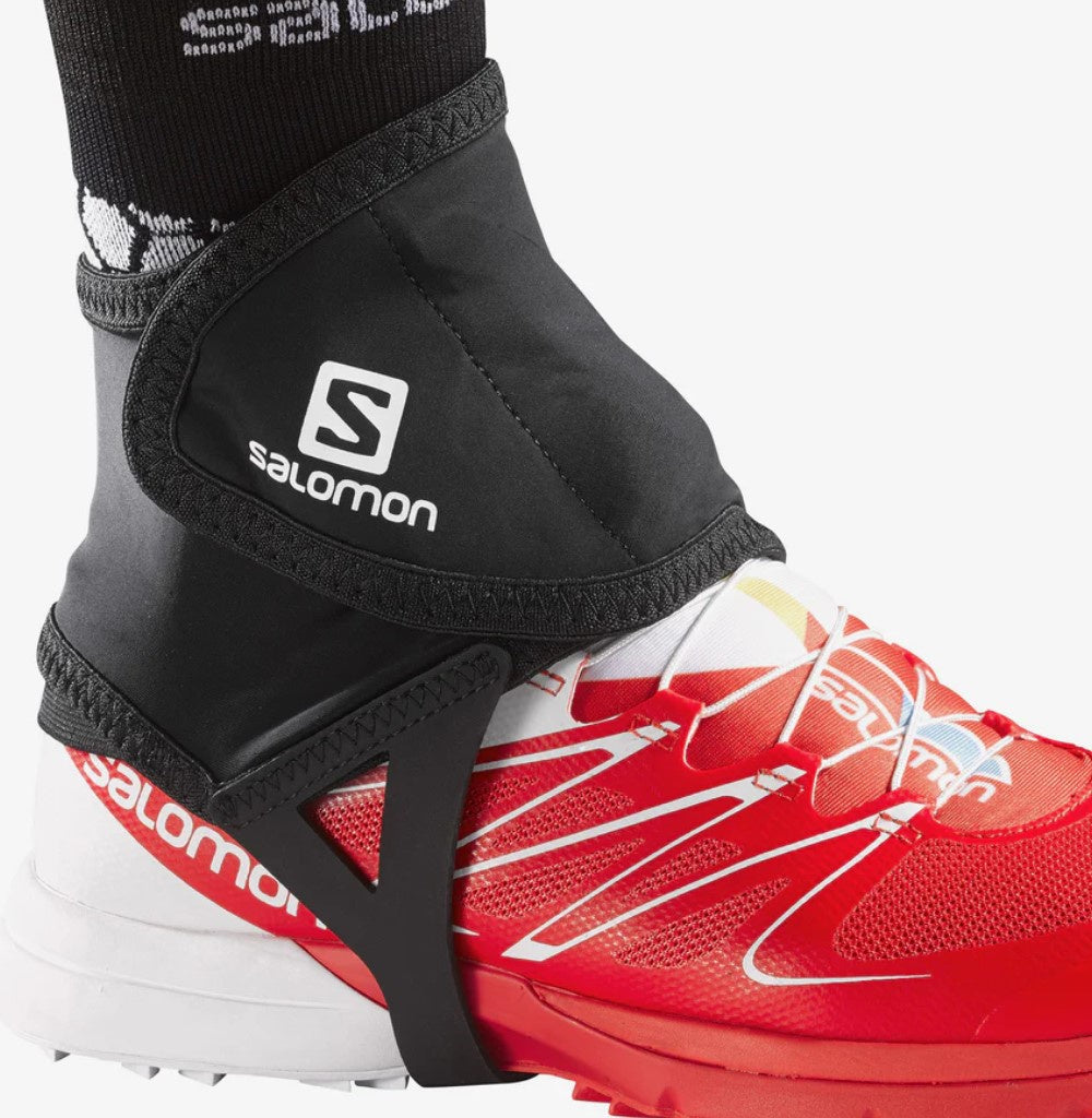 A pair of black Salomon trail gaiters worn over red hiking boots, designed to protect the ankles from debris.