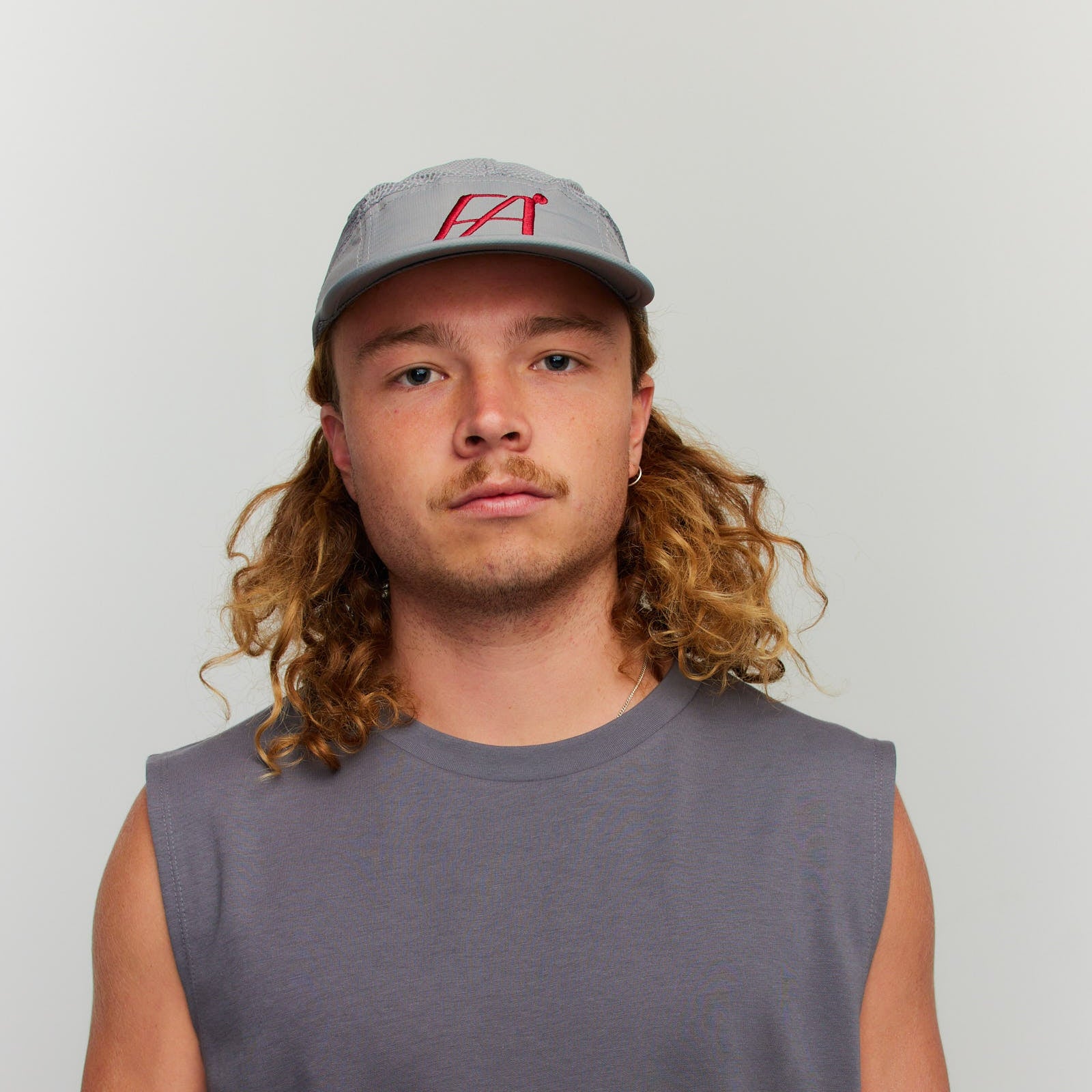 Person wearing a gray sleeveless shirt and cap with a logo on a plain background